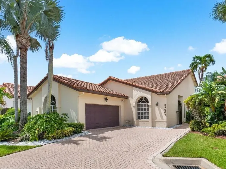 Single-story stucco home with a red tile roof, arched windows, a two-car garage and tall palms at 23065 Via Stel, Boca Raton, FL 33433