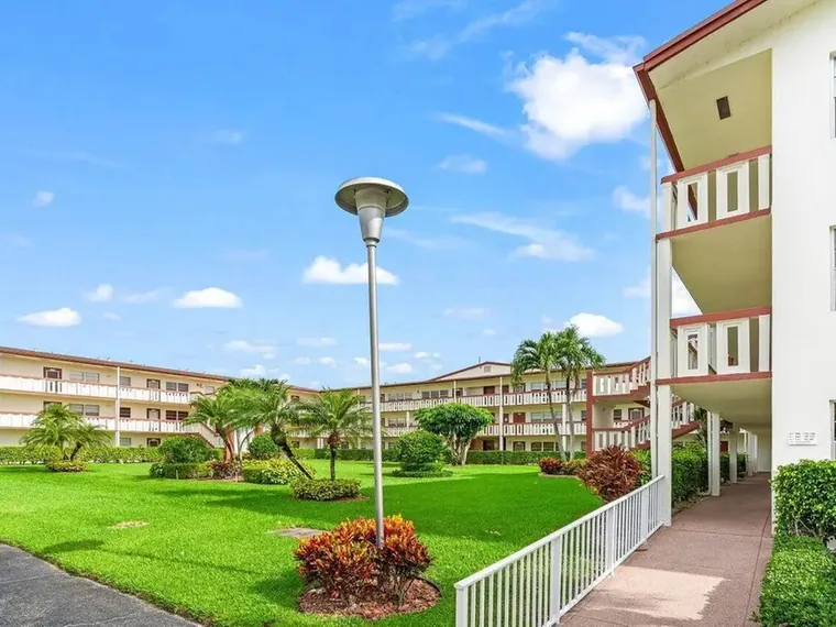 Three-story condominium buildings around a landscaped lawn with palms at 105 Brighton C, Unit 1050, Boca Raton, FL 33434